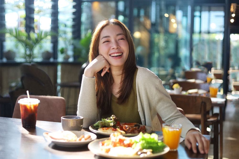 A young smiling Asian woman eating a meal at a restaurant 