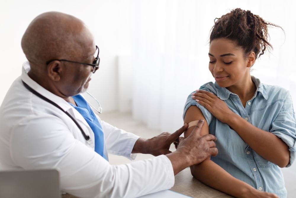  medical worker sticking plaster bandage on patient's shoulder after injection in health centre. 